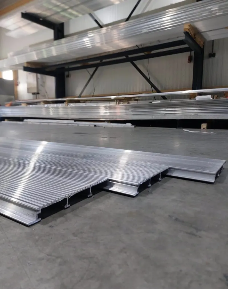 Aluminium planken met doorsnede zichtbaar, op de achtergrond stellingen met voorraad profielen