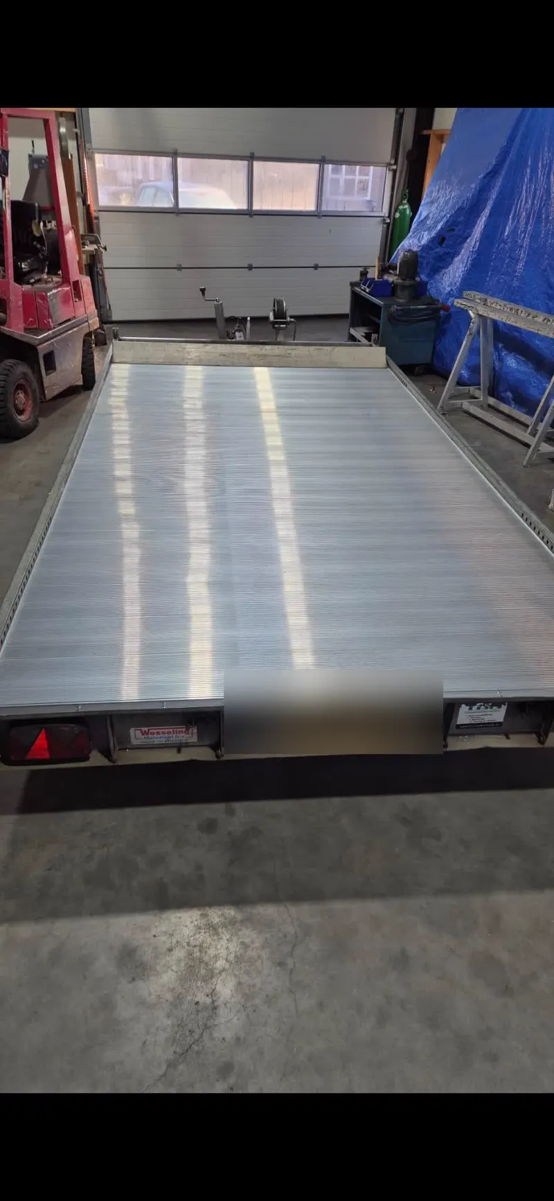 Flatbed-aanhanger met aluminium laadvloer in de werkplaats, kenteken afgeschermd