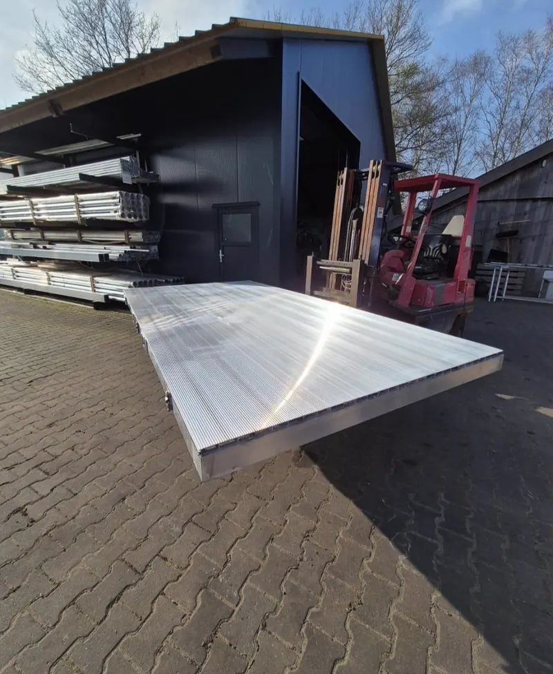 Aluminium laadvloer buiten bij de werkplaats, met een heftruck en stellingen vol profielen